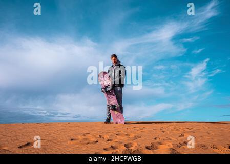 Mann mit Sandbrett auf Sanddünen in der Wüste gegen bewölkten Himmel stehen Stockfoto