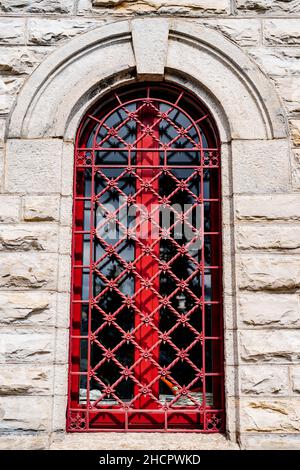 Rot geschmiedetes Gitter auf dem gewölbten Fenster eines alten Gebäudes Stockfoto