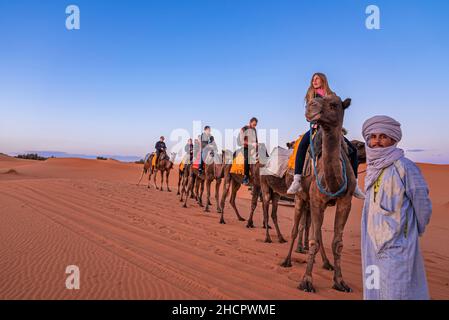 Beduinen führen Kamelkarawane mit Touristen durch den Sand in der Wüste Stockfoto