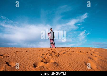 Mann mit Sandbrett auf Sanddünen in der Wüste gegen bewölkten Himmel stehen Stockfoto