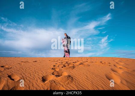 Mann mit Sandbrett auf Sanddünen in der Wüste gegen bewölkten Himmel stehen Stockfoto