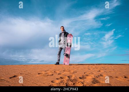 Mann mit Sandbrett auf Sanddünen in der Wüste gegen bewölkten Himmel stehen Stockfoto