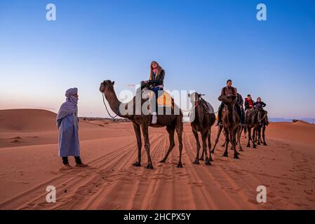 Beduinen führen Kamelkarawane mit Touristen durch den Sand in der Wüste Stockfoto