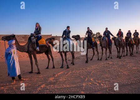 Beduinen in traditioneller Kleidung, die Touristen auf Kamelen zum Ausreiten führen Stockfoto