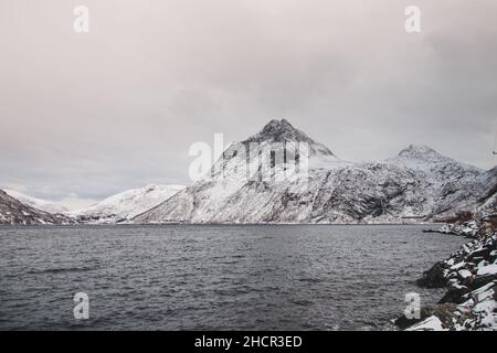 Blick vom abgelegenen Dorf Husoy auf der Insel Senja, Norwegen. Ein sehr einsames Fischerdorf. Ein Blick auf das stürmische norwegische Meer und die Schneekappe Stockfoto