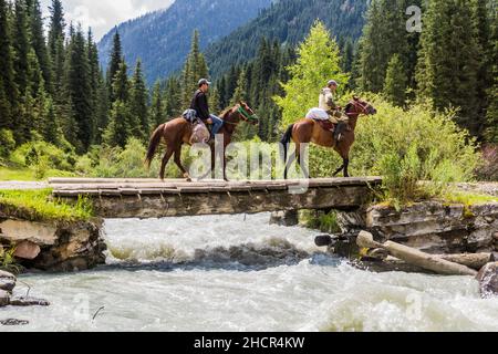 KARAKOL, KIRGISISTAN - 16. JULI 2018: Lokale Reiter überqueren eine Brücke über den Fluss Karakol in Kirgisistan Stockfoto