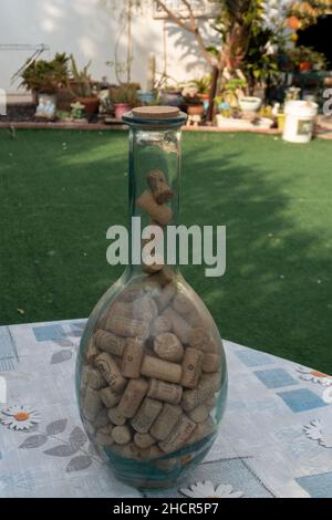 Eine große Flasche, die auf dem Tisch im Garten steht, ist bis zum Hals voll mit Weinkorken Stockfoto