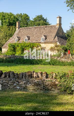 Vor einem traditionellen Steinhaus im Cotswold-Dorf Taynton, Oxfordhire, Großbritannien, blühen Hollyhocks Stockfoto