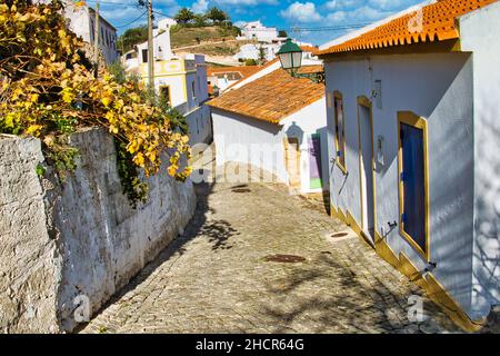 Steile Kopfsteinpflasterstraße mit weiß getünchten Häusern in der Altstadt von Aljezur, Algarve, Portugal Stockfoto