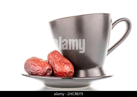 Zwei süße getrocknete ziziphus-Beeren auf einer Untertasse mit einer schwarzen Tasse, Nahaufnahme, isoliert auf Weiß. Stockfoto