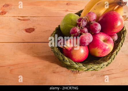 Verschiedene bunte Früchte in einem Korb gehalten. apfel, Granatapfel, Traube, Beere, Banane, Guava zusammen gehalten. Nahaufnahme. Copy Space Hintergrund. Stockfoto