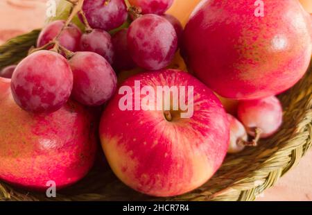 Verschiedene bunte Früchte in einem Korb gehalten. apfel, Granatapfel, Traube, Beere, Banane, Guava zusammen gehalten. Nahaufnahme. Copy Space Hintergrund. Stockfoto