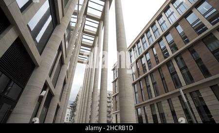 Fassade eines Gebäudes mit Marmorsäulen. Blick von unten auf einen modernen architektonischen Komplex, ein neues Gebäude mit hellbeigen Säulen und großen Fenstern. Stockfoto