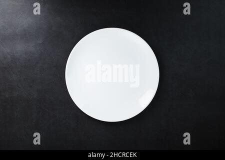 Weiße Platte auf schwarzem Hintergrund, Draufsicht. Minimalistisches Konzept Stockfoto
