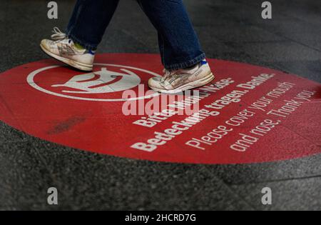 Großer runder Kreis auf dem Bahnsteigboden des Marienplatz-Bahnhofs in München mit dem Wunsch, Mund und Nase zu bedecken. Die Füße der Passagiere sind zu sehen. Stockfoto