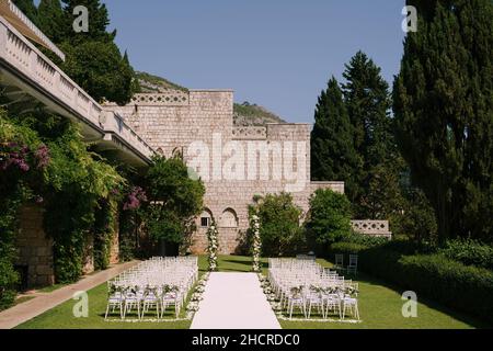 Zwischen den Stuhlreihen verläuft ein weißer Teppich zum Halbbogen der Hochzeit im Garten Stockfoto