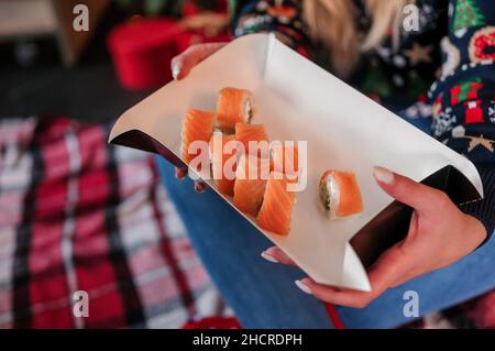 Eine Schachtel Sushi in den Händen eines Mädchens auf dem Hintergrund eines Weihnachtsbaums Stockfoto