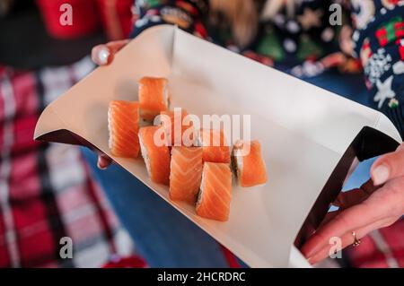 Eine Schachtel Sushi in den Händen eines Mädchens auf dem Hintergrund eines Weihnachtsbaums Stockfoto