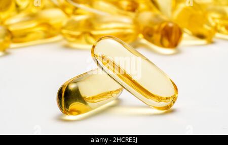 Zwei Kapseln Omega 3 und viele andere Kapseln auf verschwommenem Hintergrund. Image des Gesundheitskonzepts Stockfoto