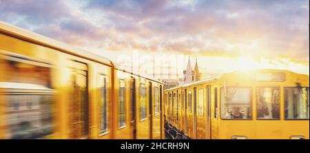 Berliner U-Bahn mit Oberbaumbrücke im Hintergrund im goldenen Abendlicht bei Sonnenuntergang mit dramatischen Wolken, Berlin Friedrichshain-Kreuzberg Stockfoto