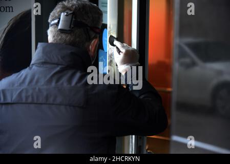 Vendrell, Spanien. 31st Dez 2021. Ein Agent der katalanischen Polizei-Diebstahluntersuchungsgruppe sucht an der Eingangstür des Bankbüros der CaixaBank nach den Fingerabdrücken des Räubers.Ein Mann mit einem Messer führt einen Raub in einem Büro der Bank CaixaBank in El Vendrell (Tarragona, Spanien) durch. Flucht mit einer Sammlung, die noch von den Bankverantwortlichen bestimmt werden muss. Die katalanische Polizei untersucht den Ort des Raubüberfalls und sucht nach Fingerabdrücken des Räubers Credit: SOPA Images Limited/Alamy Live News Stockfoto