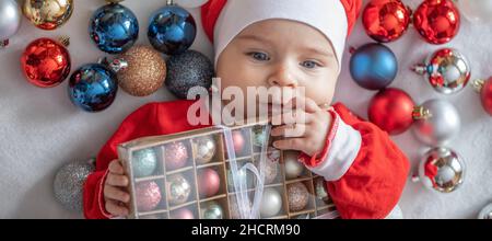 Kleinkind im Anzug des Weihnachtsmannes mit Weihnachtsbaumschmuck. Stockfoto