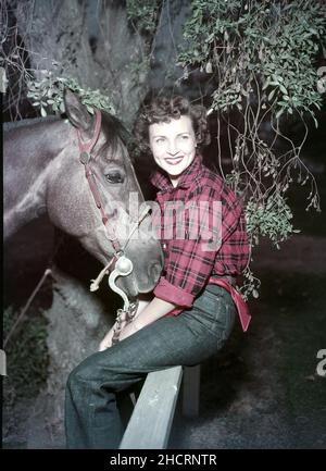 Um 1957, Hollywood, Kalifornien, USA: Lächelnde amerikanische Schauspielerin und Komikerin BETTY WHITE mit einem Pferd, während sie mit rot kariertem Hemd und Jeans auf einem Zaun sitzt. (Bild: © Globe Photos/ZUMA Press Wire) Stockfoto