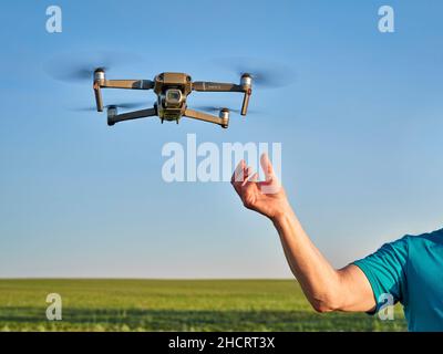 New Raymer, CO, USA - 8. Juni 2021: Eine Pilot Hand und eine DJI Mavic 2 Pro Quadcopter Drohne fliegen über grüne Prärie. Stockfoto