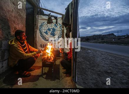 Gaza, Palästina. 31st Dez 2021. Eine palästinensische Familie sitzt am Feuer, um sich vor ihrem Haus bei kaltem Wetter am Rande des Flüchtlingslagers Khan Yunis aufzuwärmen. (Foto von Yousef Masoud/SOPA Images/Sipa USA) Quelle: SIPA USA/Alamy Live News Stockfoto