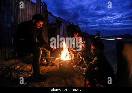 Gaza, Palästina. 31st Dez 2021. Eine palästinensische Familie sitzt am Feuer, um sich vor ihrem Haus bei kaltem Wetter am Rande des Flüchtlingslagers Khan Yunis aufzuwärmen. (Foto von Yousef Masoud/SOPA Images/Sipa USA) Quelle: SIPA USA/Alamy Live News Stockfoto