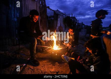 Gaza, Palästina. 31st Dez 2021. Eine palästinensische Familie sitzt am Feuer, um sich vor ihrem Haus bei kaltem Wetter am Rande des Flüchtlingslagers Khan Yunis aufzuwärmen. (Foto von Yousef Masoud/SOPA Images/Sipa USA) Quelle: SIPA USA/Alamy Live News Stockfoto