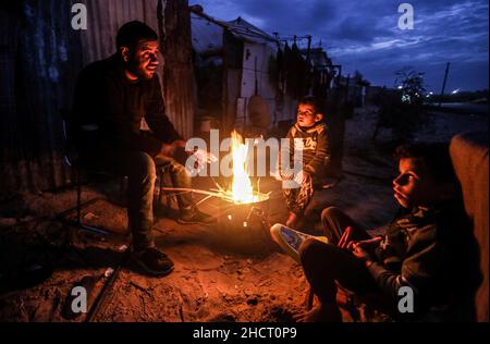 Gaza, Palästina. 31st Dez 2021. Eine palästinensische Familie sitzt am Feuer, um sich vor ihrem Haus bei kaltem Wetter am Rande des Flüchtlingslagers Khan Yunis aufzuwärmen. (Bild: © Yousef Masoud/SOPA Images via ZUMA Press Wire) Bild: ZUMA Press, Inc./Alamy Live News Stockfoto