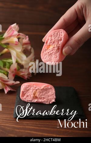 Frau hält ein Stück leckere Erdbeer-Mochi auf Holzhintergrund Stockfoto