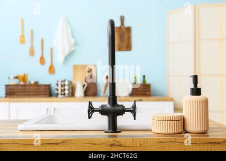 Schwarzer Wasserhahn und Spülmittel auf Holztischplatte in der Küche Stockfoto