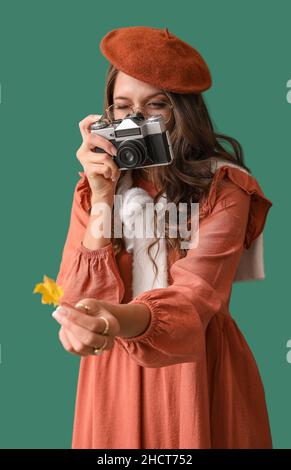 Schöne Pariser Frau, die das Herbstblatt auf grünem Hintergrund fotografiert Stockfoto