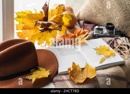 Schöne Komposition mit geöffnetem Buch, Filzhut und herbstlicher Dekoration auf Fensterbank Stockfoto