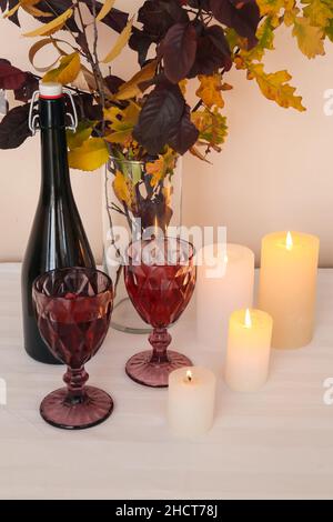 Vase mit Herbstzweigen, Flasche Wein, Gläser und brennende Kerzen auf dem Tisch, Nahaufnahme Stockfoto