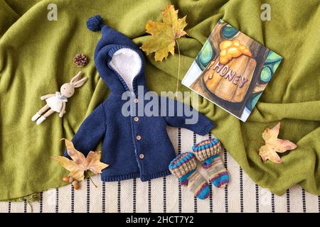 Babykleidung, Spielzeug Kaninchen, Buch und Herbst Dekor auf farbigem Stoff Hintergrund Stockfoto