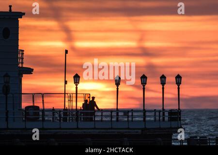 Worthing Beach, Worthing, Großbritannien. 1st Januar 2022. Die Menschen stehen am Ende des Worthing Pier und beobachten, wie die Sonne am ersten Tag des 2022. September über dem Worthing Pier aufgeht. Bild nach Kredit: Julie Edwards/Alamy Live News Stockfoto