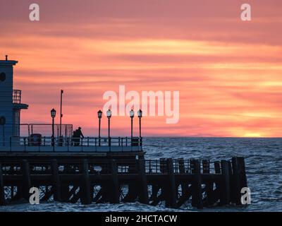 Worthing Beach, Worthing, Großbritannien. 1st Januar 2022. Die Menschen stehen am Ende des Worthing Pier und beobachten, wie die Sonne am ersten Tag des 2022. September über dem Worthing Pier aufgeht. Bild nach Kredit: Julie Edwards/Alamy Live News Stockfoto