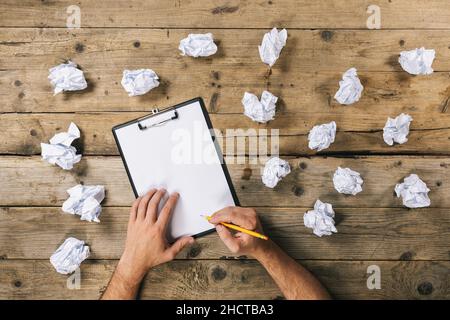 Hände halten Zwischenablage und schreiben Mock-up oder Ideen mit zerknitterten Papierkugeln. Brainstorming-Konzept-Image Stockfoto