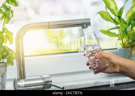 Frau, die in der Küche Glas mit Wasser aus dem Wasserhahn füllte Stockfoto