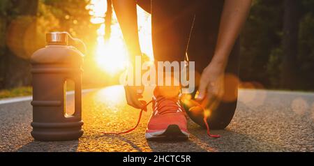 Läuferin Frau, die mit Trinkflasche Laufschuhe versucht, sich zum Laufen bereit zu machen. Gesunder Lebensstil. Workout- und Diät-Konzept. Stockfoto