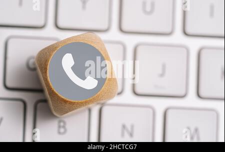 Telefonsymbol auf einem Holzwürfel auf einer Tastatur. Kontakt- und Kommunikationsmethoden Konzeptbild Stockfoto