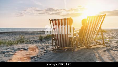 Glückliches romantisches Paar, das den wunderschönen Sonnenuntergang am Strand genießt und mit Wein toastet Stockfoto