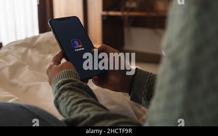 Frau, die eine iPhone XS Opening Face App am Bett hält, ist faceapp eine beliebte Fotobearbeitungs-Anwendung im App Store. Stockfoto