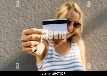Porträt einer hübschen jungen Frau in Pullover mit Kreditkarte im Gesicht gekleidet. Copyspace für Ihren individuellen Text. Stockfoto