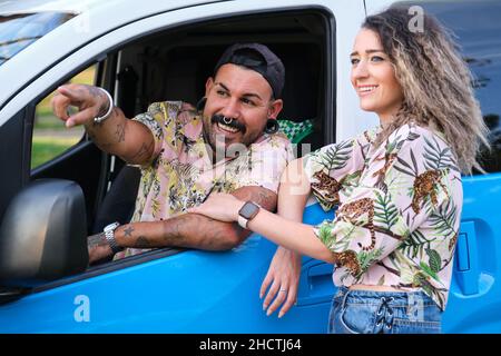 Das junge tätowierte Paar lächelte mit dem Van, der nach vorne zeigte. Stockfoto