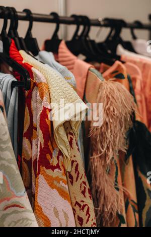 Designer-Mode-Outfits hängen in einer Reihe auf der Backstage der Fashion Week. Vertikal Stockfoto