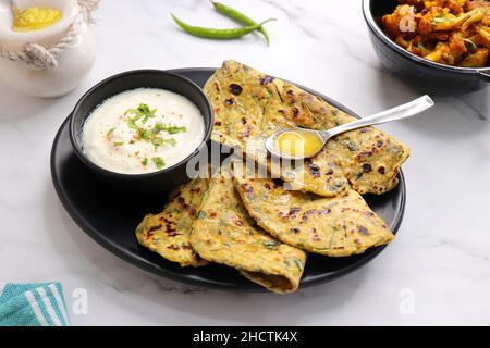 Ein Essen namens Methi Paratha oder Methi Thepla ist ein indisches Frühstücksgericht mit Quark und einem Löffel voller Desi Ghee serviert. Stockfoto